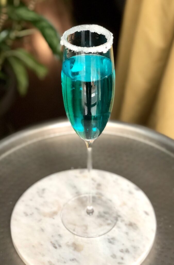 Blue Christmas Prosecco cocktail on a marble trivet and metal table.