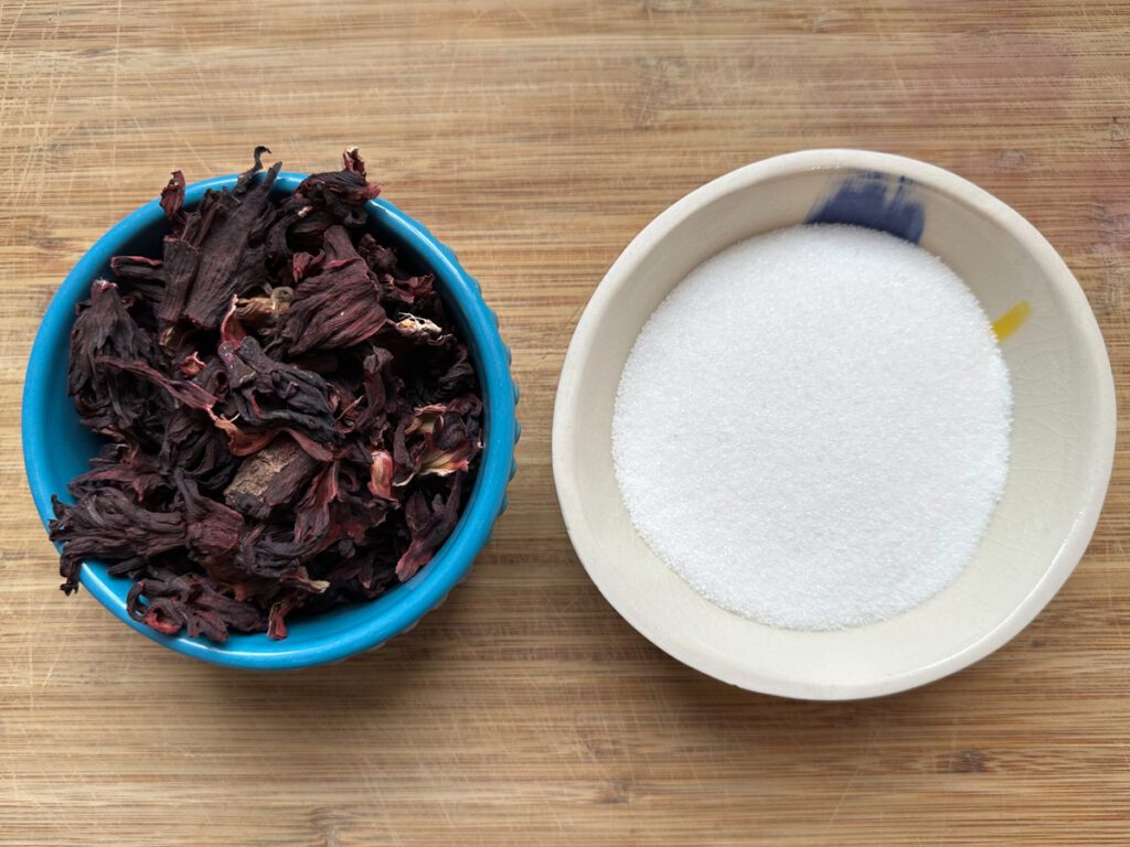 Two bowls one with dried hisbiscus leaves (sorrel) and the other with white sugar. 