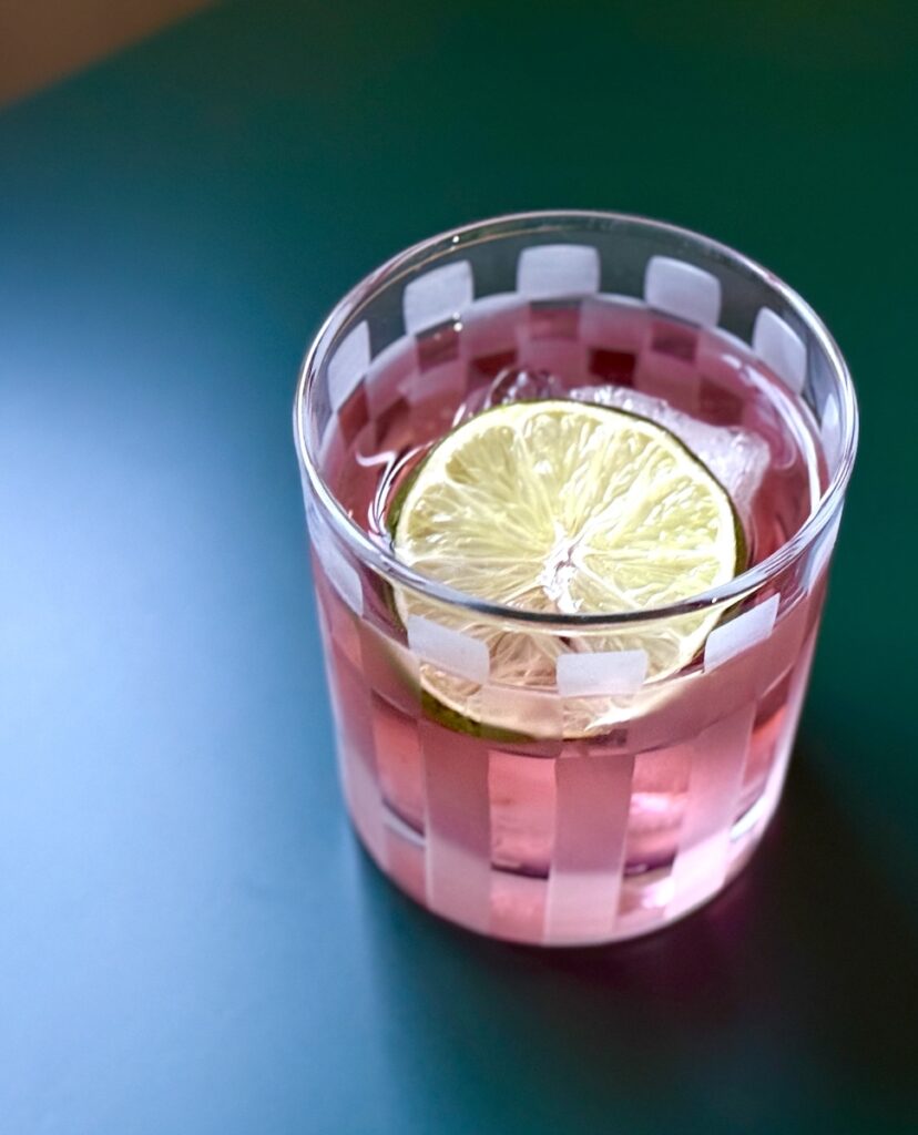 Pink Negroni Cocktail garnished with a lime wedge sitting on a green table.